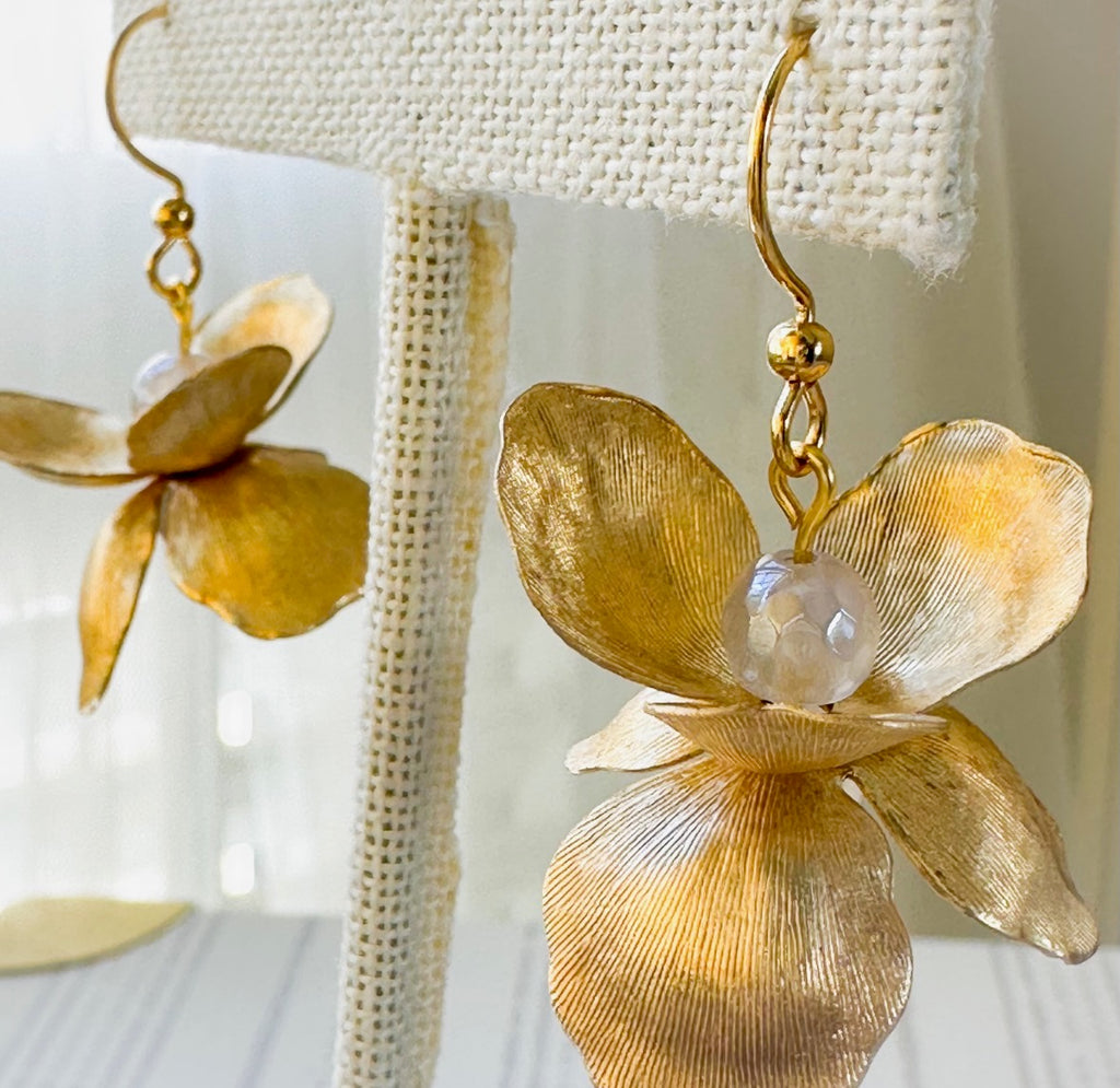 Gold flower-shaped earrings with a pearl center on a textured white background