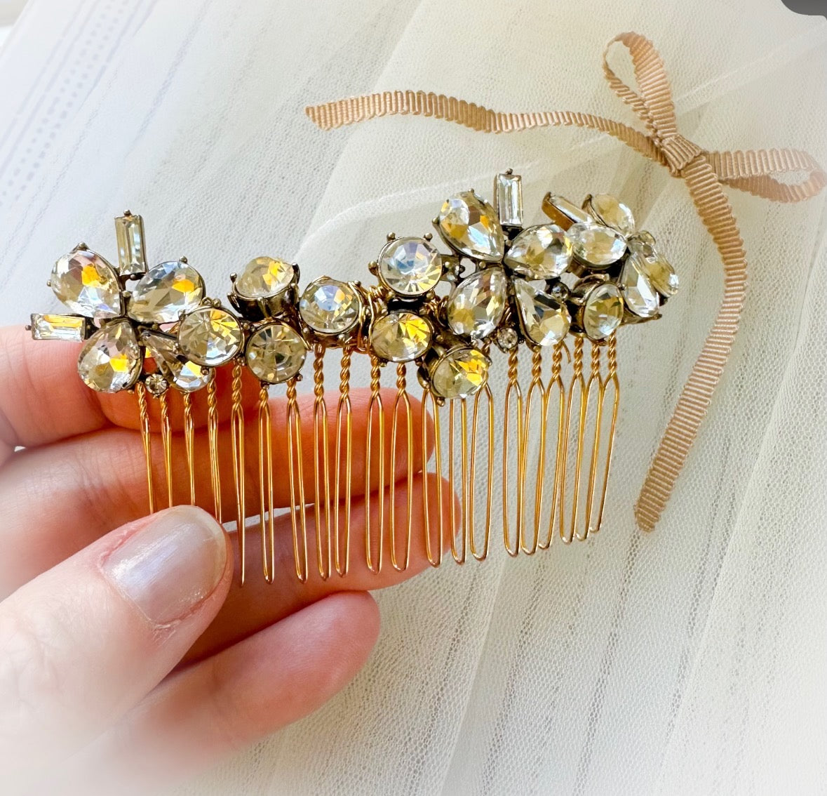 Decorative hair comb with crystals held by a hand on a light background