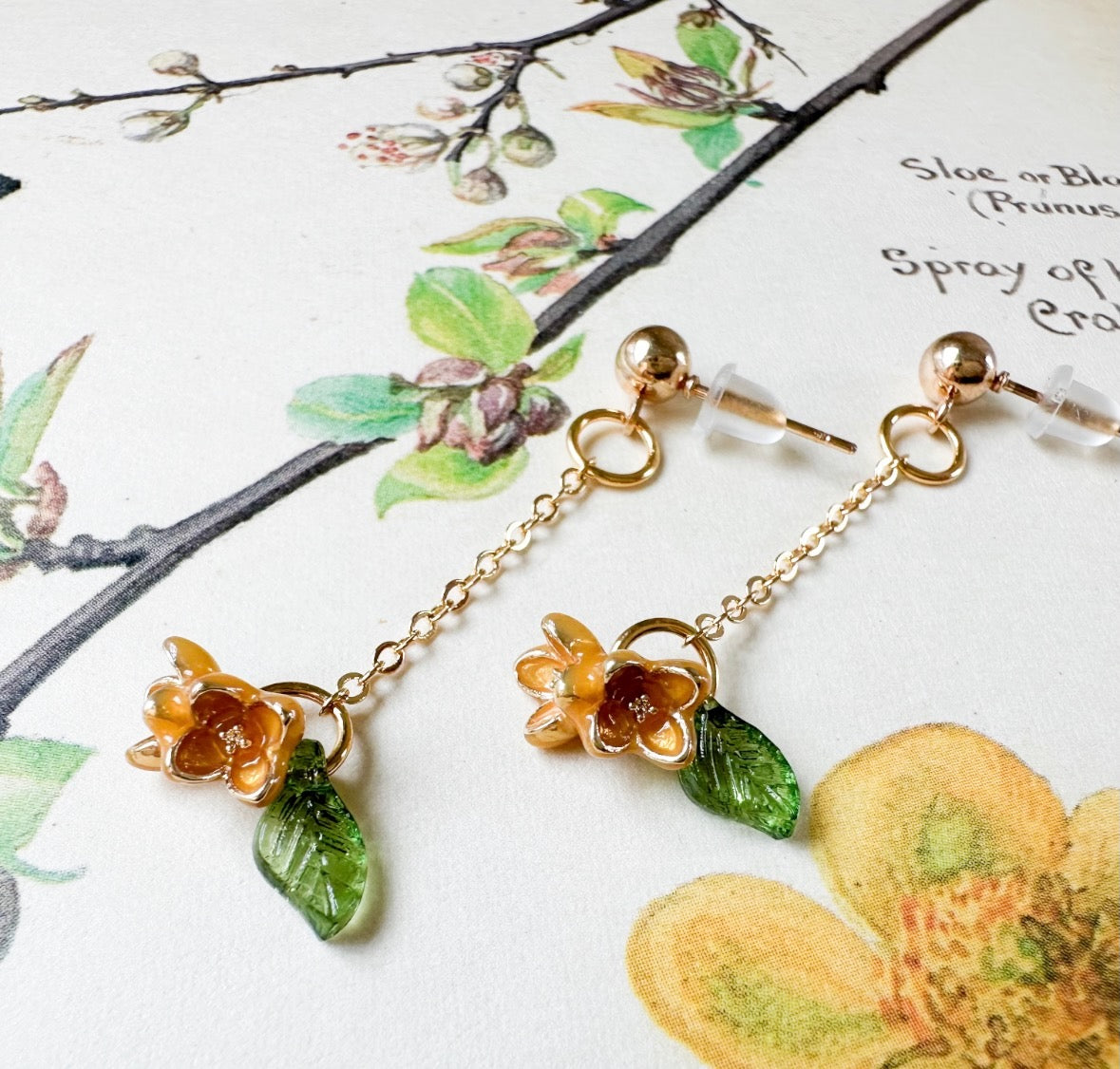 Gold floral earrings with green leaves on a floral background