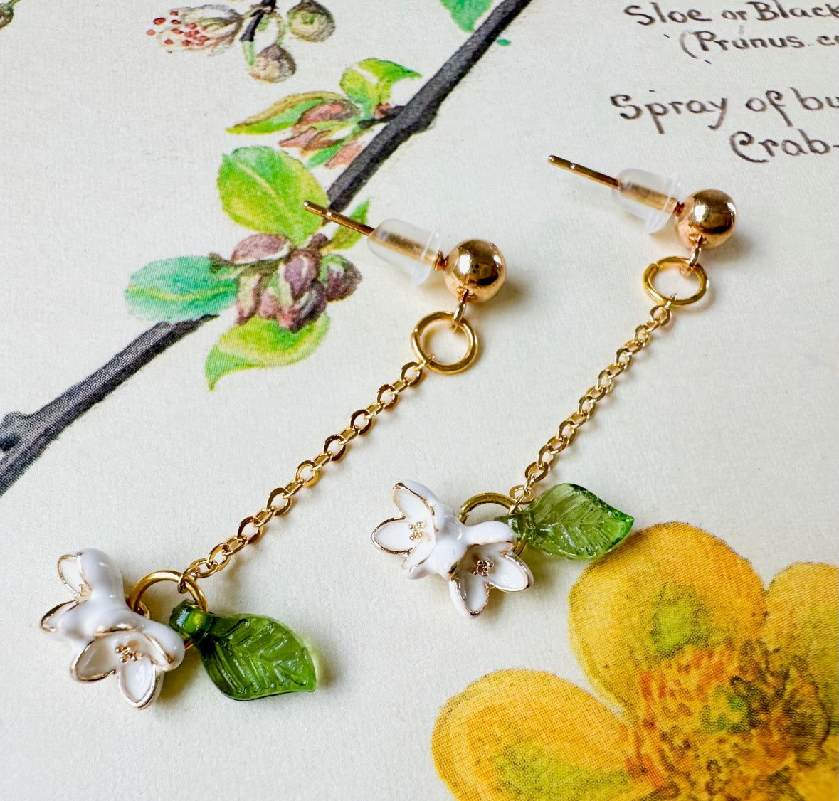 Gold earrings with floral charms on a botanical illustration background