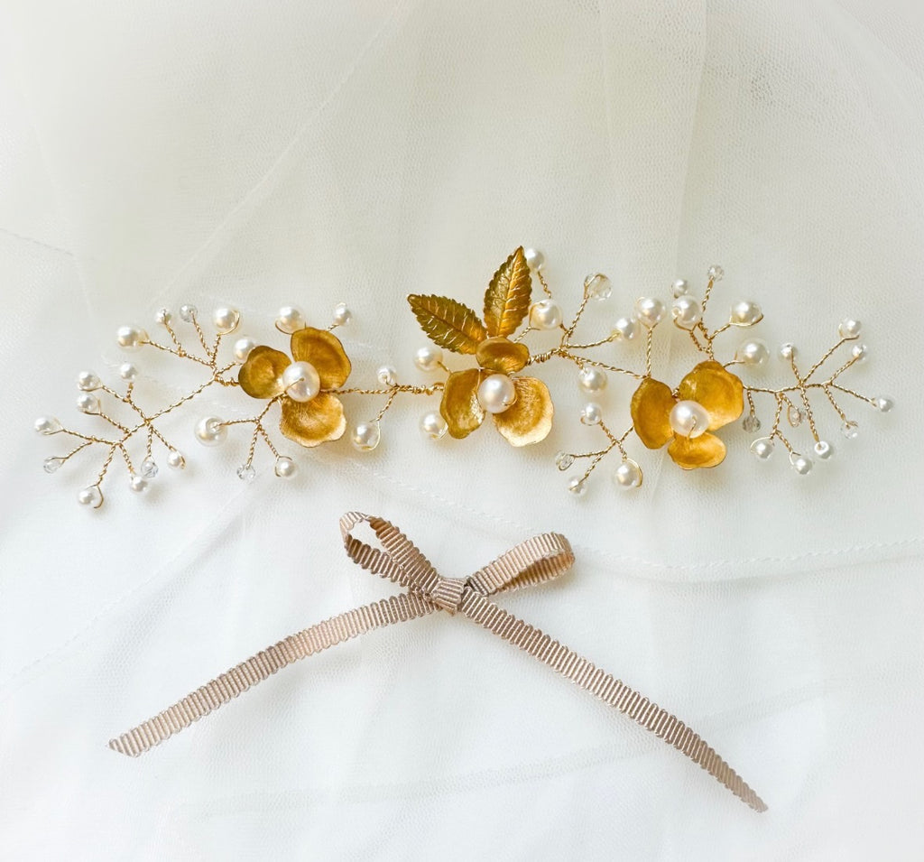 Gold floral hairpiece with pearls and a gold brass flower on a light background