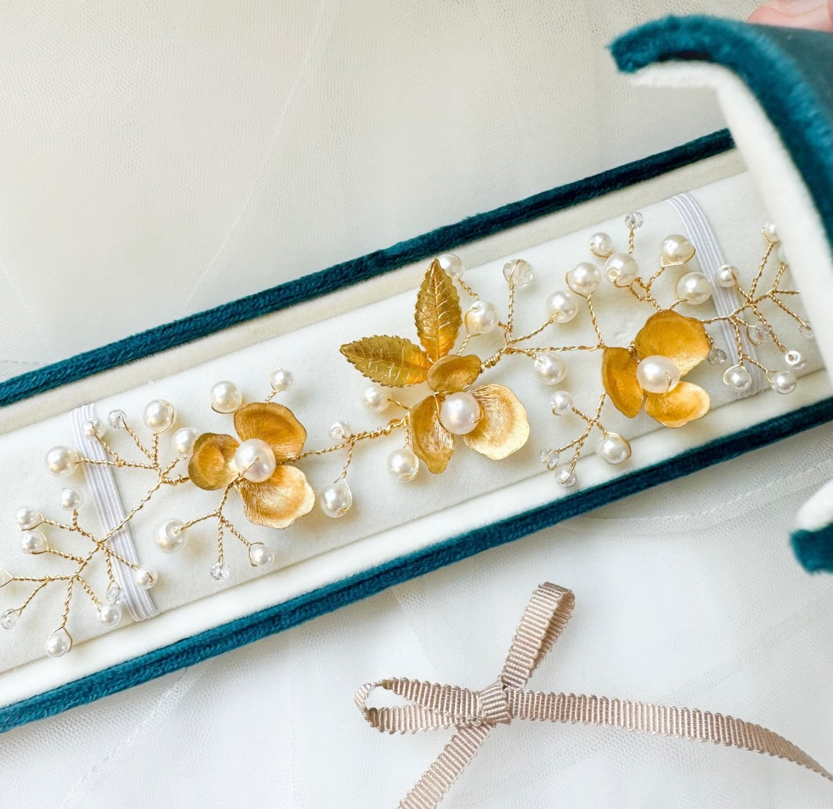 Decorative hair accessory with gold leaves and pearls on a white background lay in a blue velvet keepsake box.