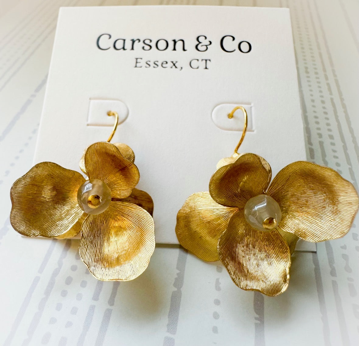 Gold flower-shaped earrings on a Carson & Co card