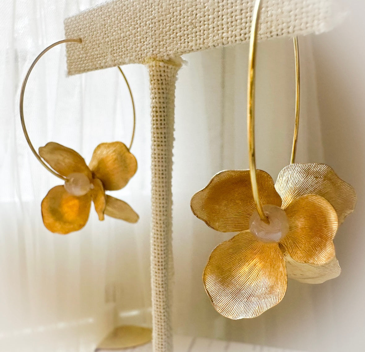 Gold flower-shaped earrings on a white stand with a blurred background