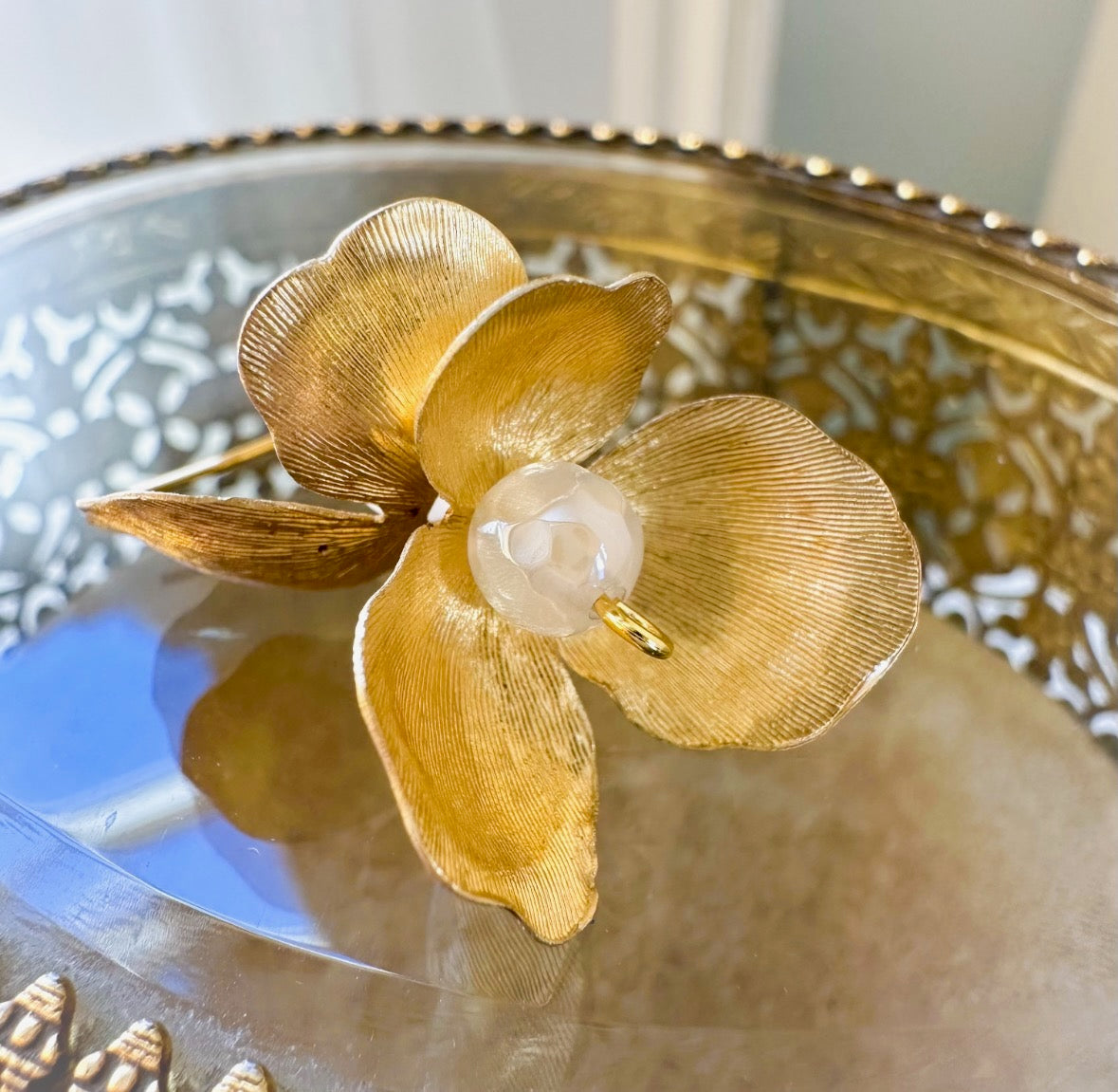 Gold flower-shaped brooch with a pearl center on a decorative plate.