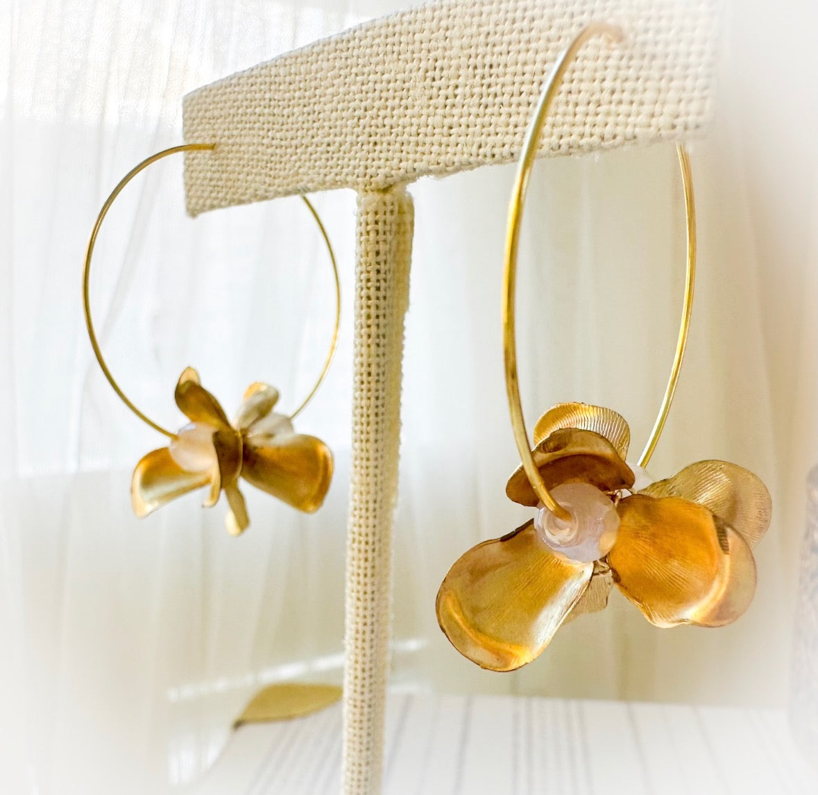 Gold hoop earrings with amber-colored floral designs on a beige stand.