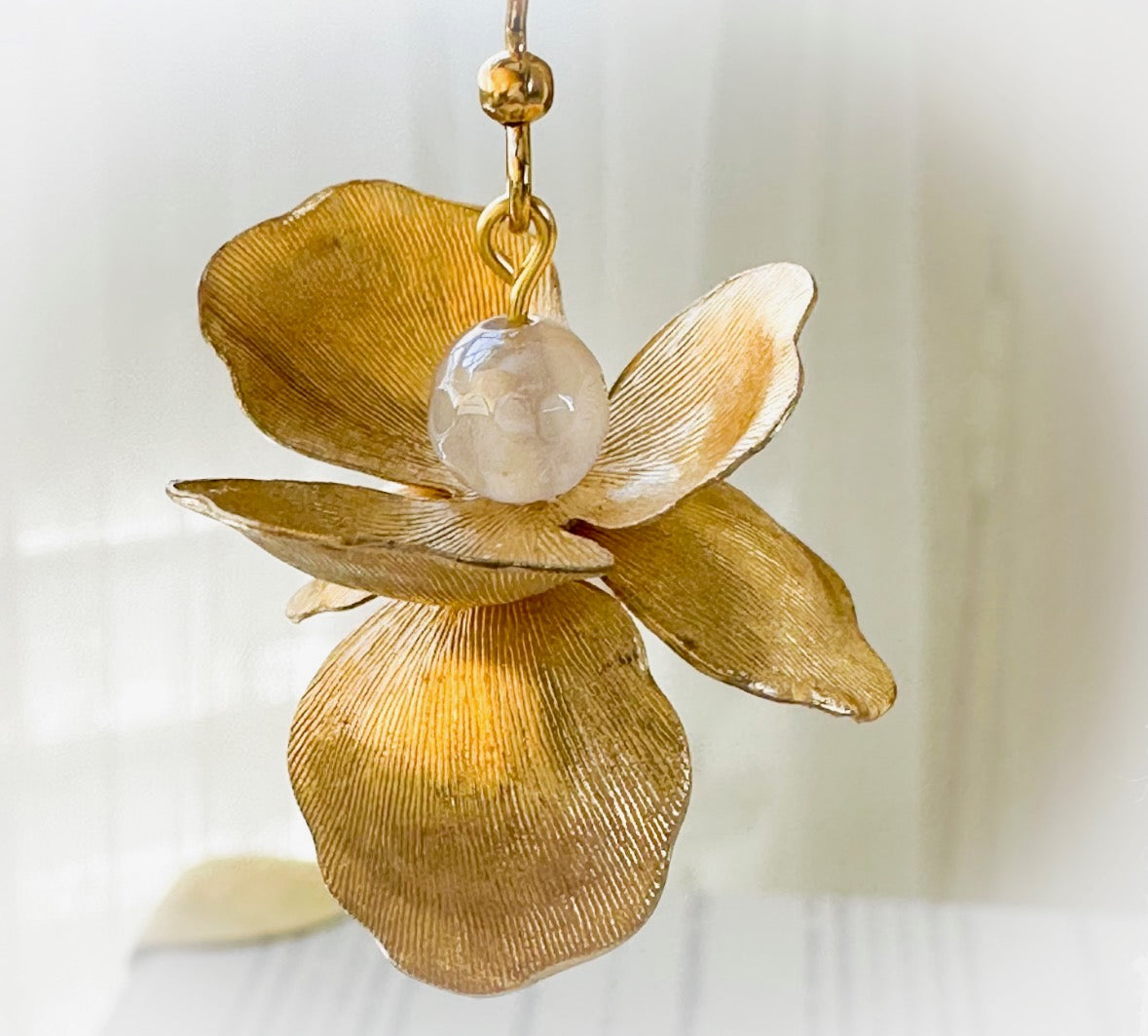 Gold flower-shaped earring with a central gemstone on a blurred background