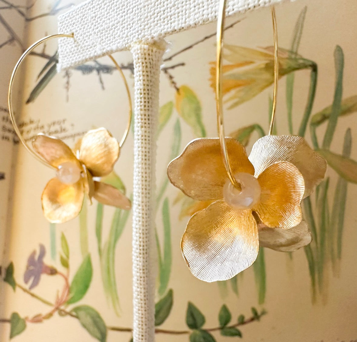 Gold floral earrings with pearl centers on a floral-patterned background