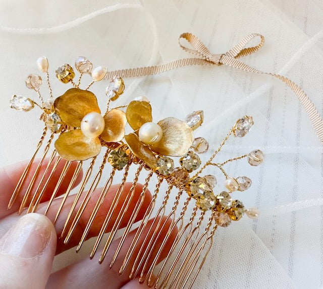 Gold hair comb with floral and crystal details held by a hand on a white background