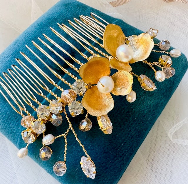 Gold hair comb with floral and crystal details on a teal cushion