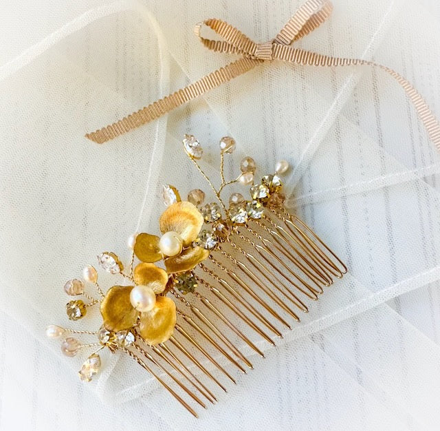 Bridal hair comb with brass flowers and pearls and rhinestones, on a veil background.